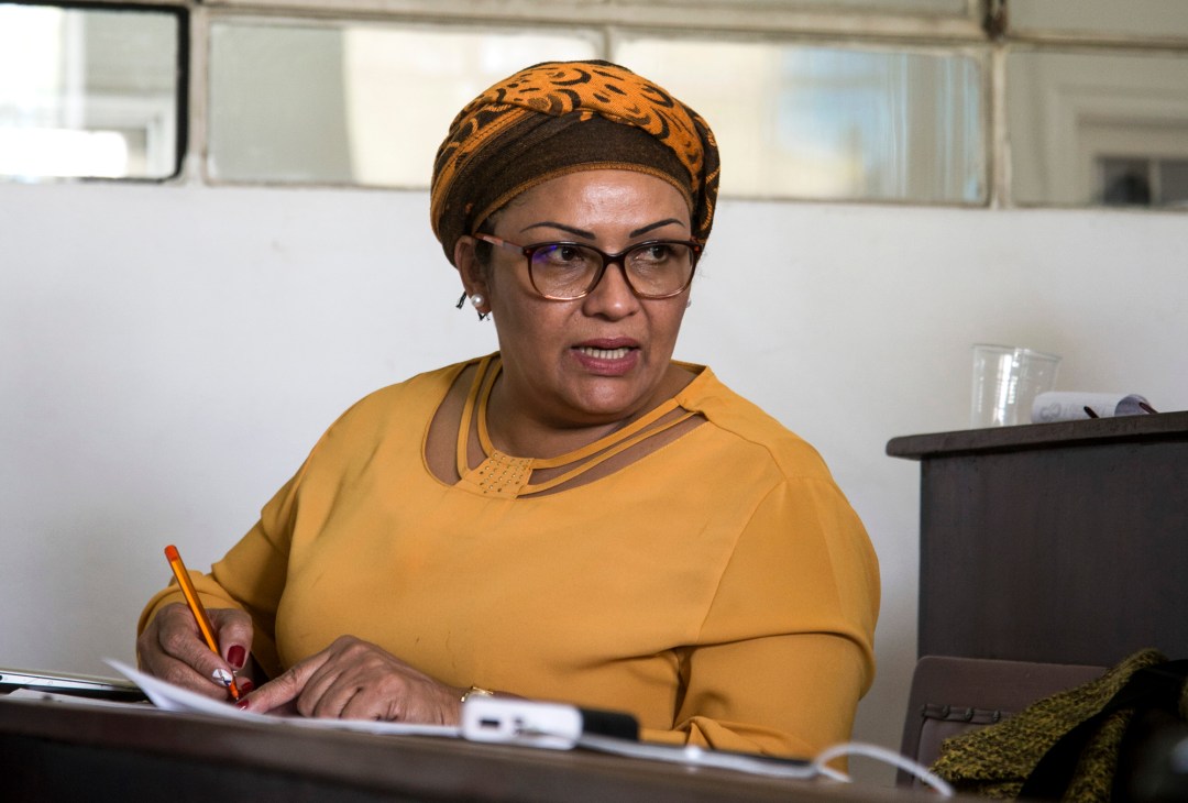 Woman in yellow top and patterned headwrap sitting at desk with pen and papers