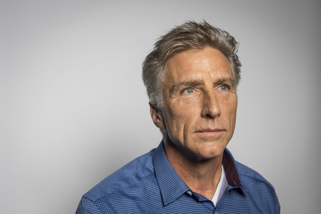 Portrait of Bracken Darrell, CEO of Logitech, wearing a blue shirt against a gray background.