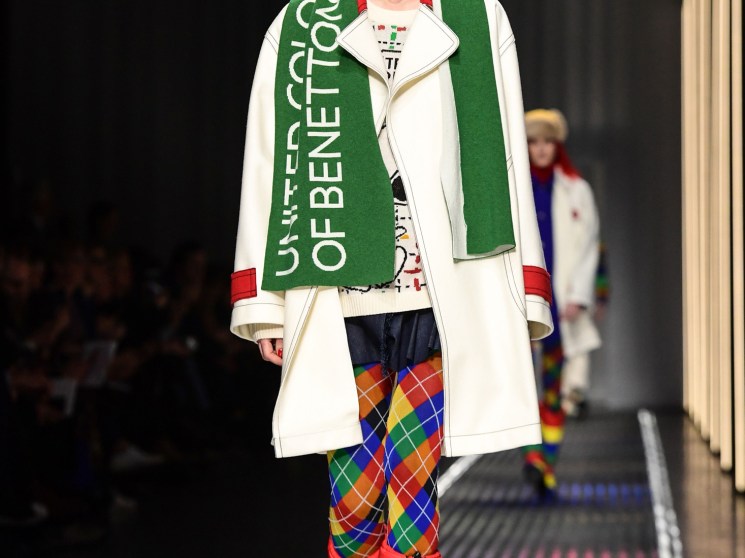 Model on runway wearing Benetton white coat with green scarf and rainbow argyle leggings.