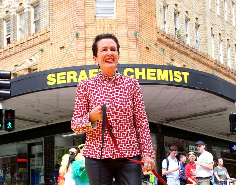 Woman in red patterned jacket smiling outside Serapis Chemist storefront on a London street.