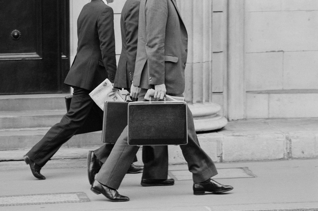 Black and white photo of businessmen in suits carrying traditional briefcases while walking on a street.