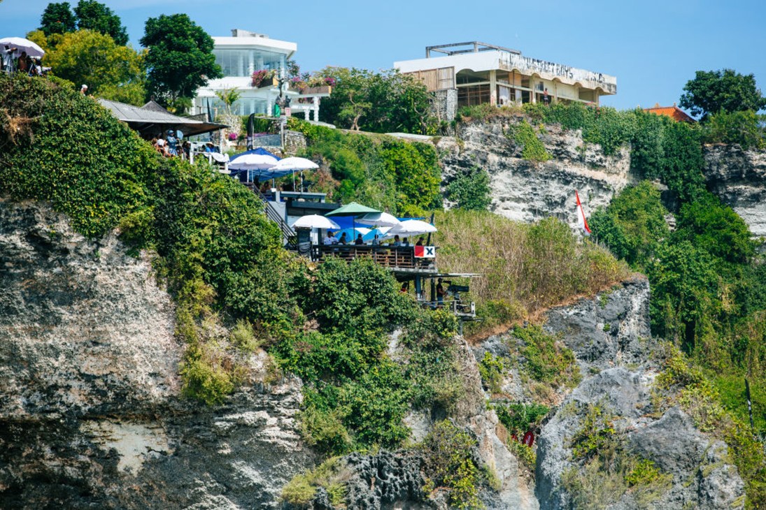 Clifftop beachside resort with modern architecture, restaurants, and umbrellas overlooking tropical coastline.