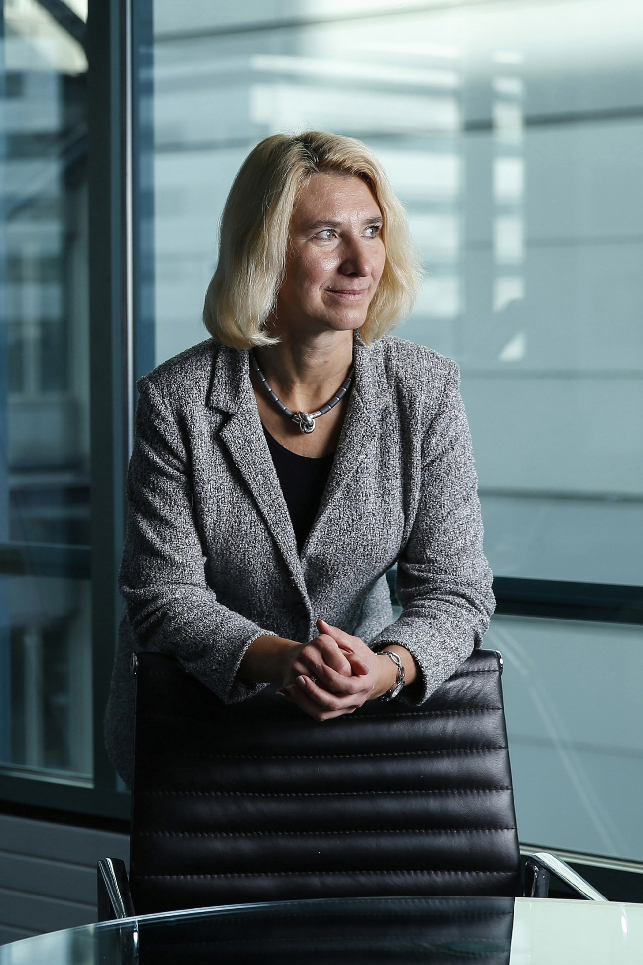 Professional woman in gray blazer sitting at conference table in modern office with glass windows