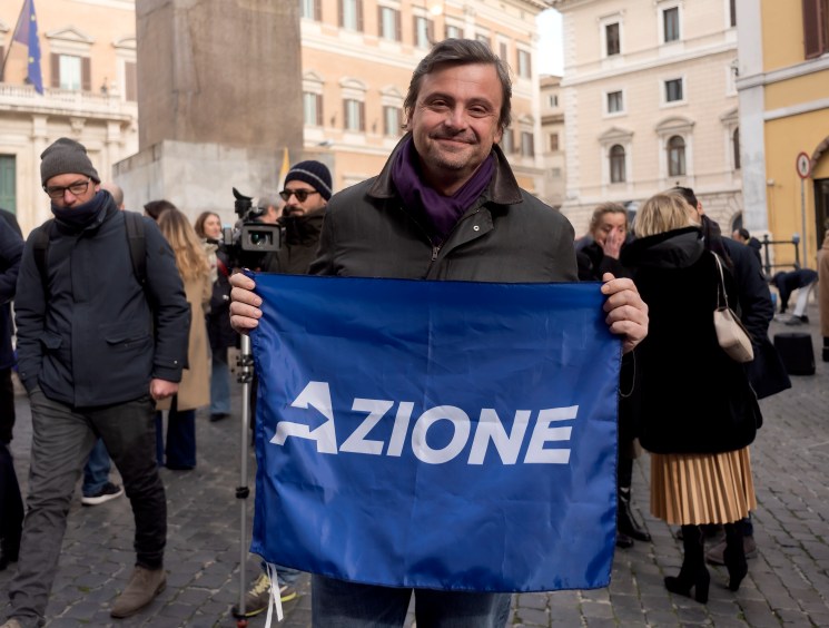 Carlo Calenda holding an Azione party flag at a Rome campaign event.