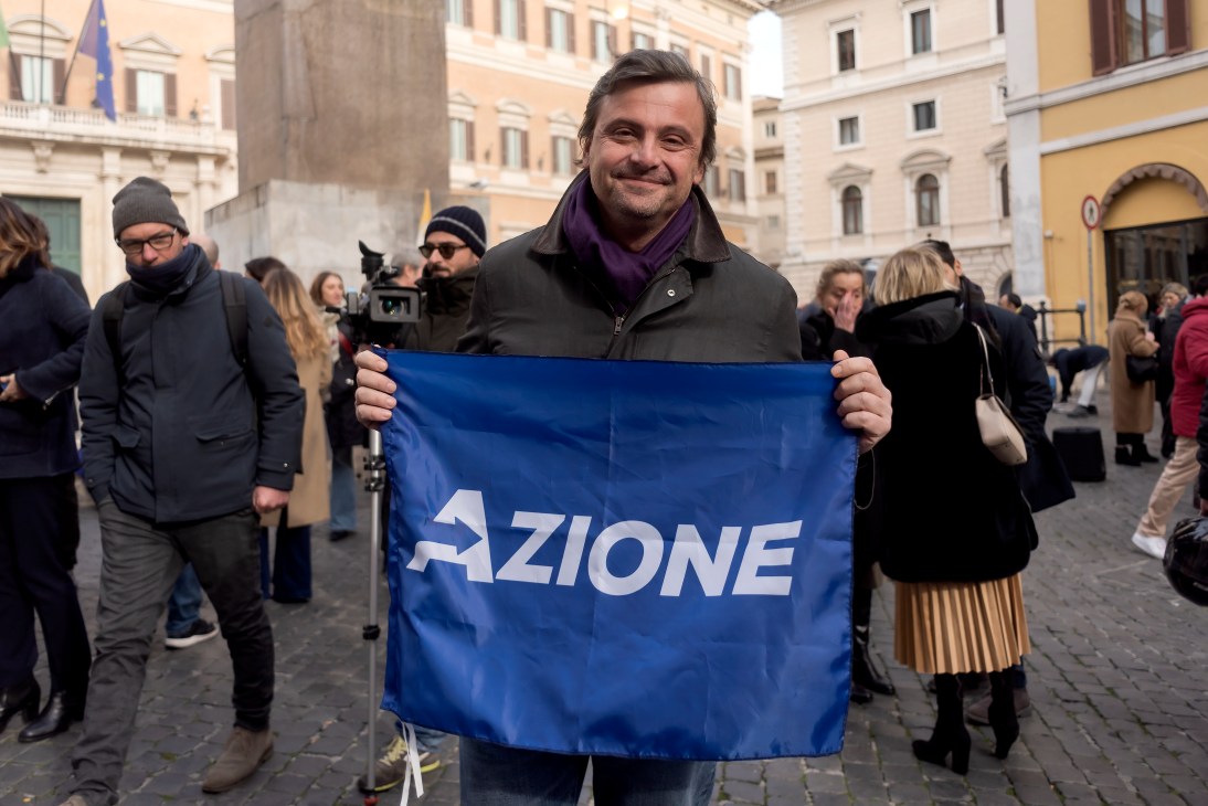 Carlo Calenda holding an Azione party flag at a Rome campaign event.