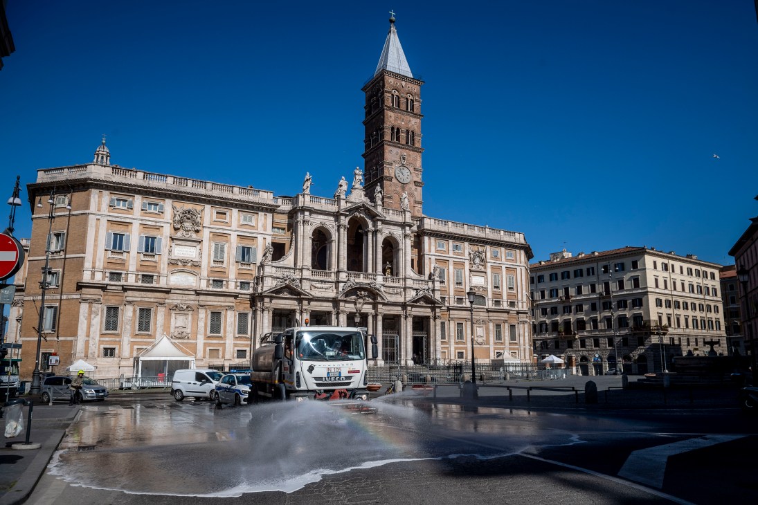 Roman basilica with bell tower and classical facade in sunny plaza with vehicles and wet pavement