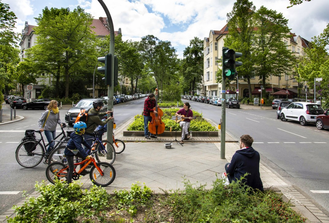 A Berlin street scene with people on bicycles and a cellist performing outdoors during pandemic lockdown.