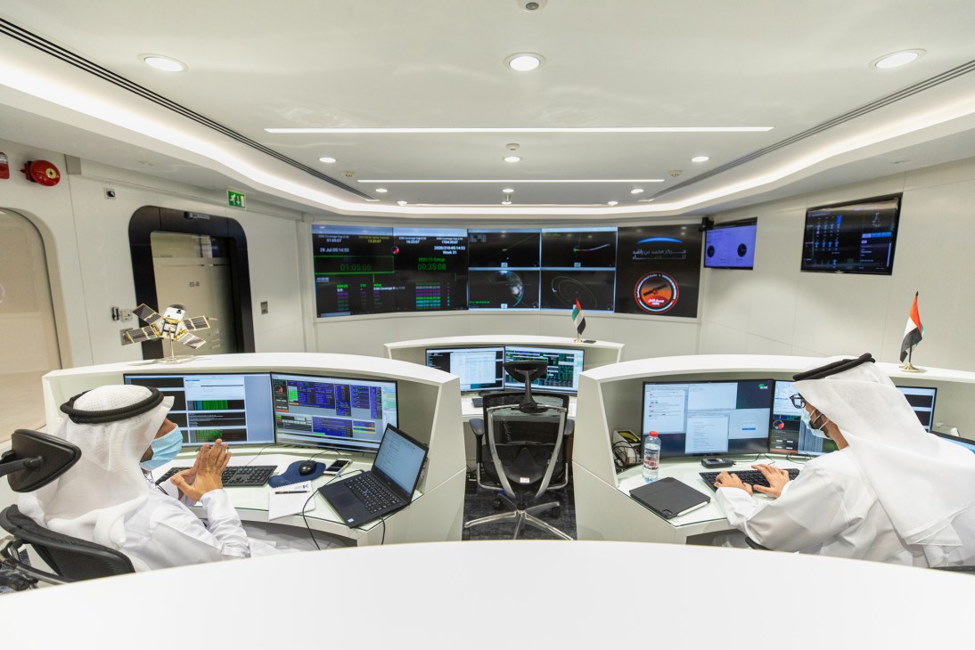 Mission control center with operators in traditional Emirati dress monitoring multiple screens and data displays