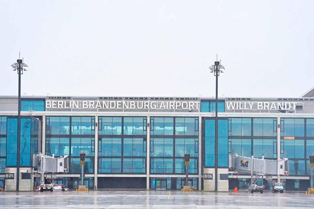 Berlin Brandenburg Airport terminal building with glass facade and signage, aircraft boarding bridges visible.