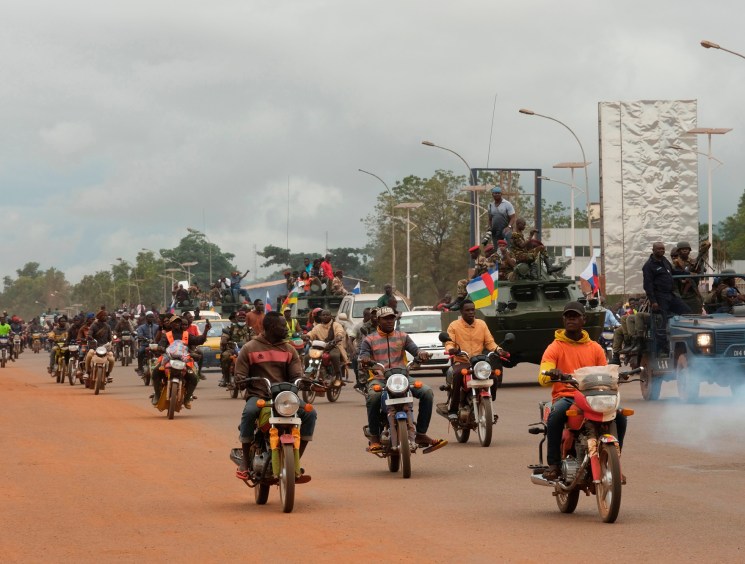 Large crowd on motorcycles and military vehicles parading down a wide street.