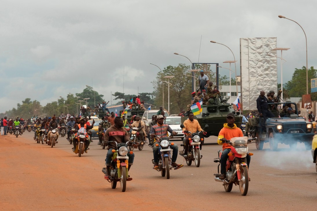 Military convoy with motorcycles, armoured vehicles and crowds on street in Central African Republic