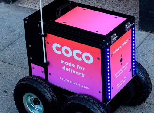 Pink Coco delivery robot with four wheels on sidewalk pavement