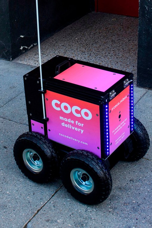 Pink Coco delivery robot with four wheels on sidewalk pavement