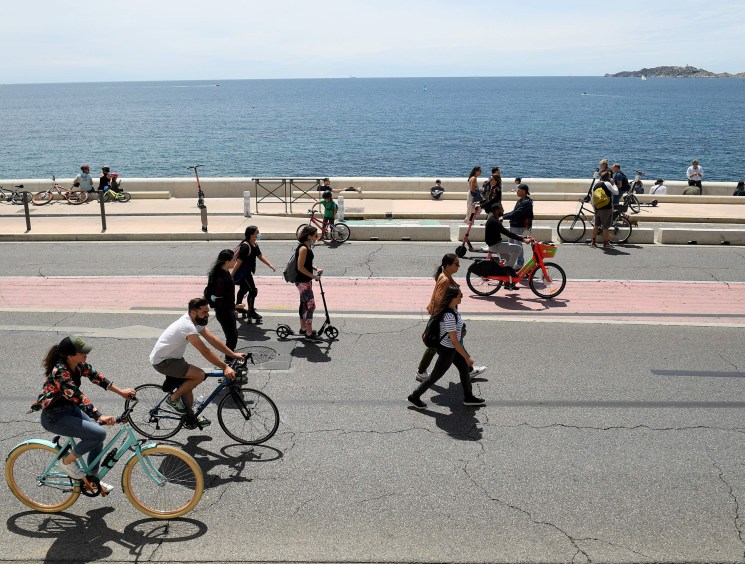 People cycling, walking and using scooters on a coastal road with Mediterranean sea in background
