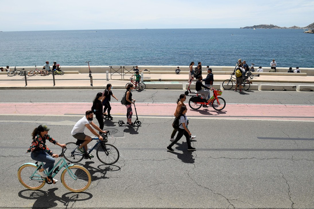 People cycling, walking and using scooters on a coastal road with Mediterranean sea in background
