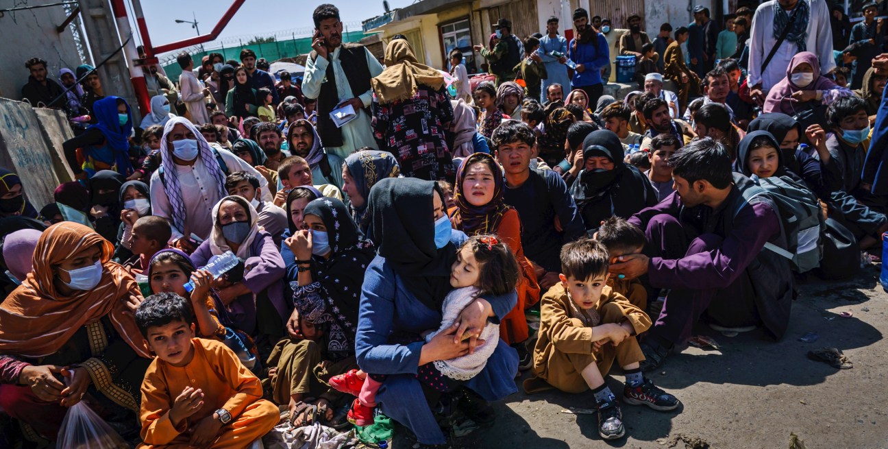 Afghan women and children crouching and waiting at Taliban checkpoint near Kabul airport entrance