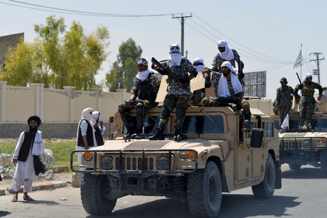 Taliban fighters armed with weapons ride on military vehicles in Afghanistan.