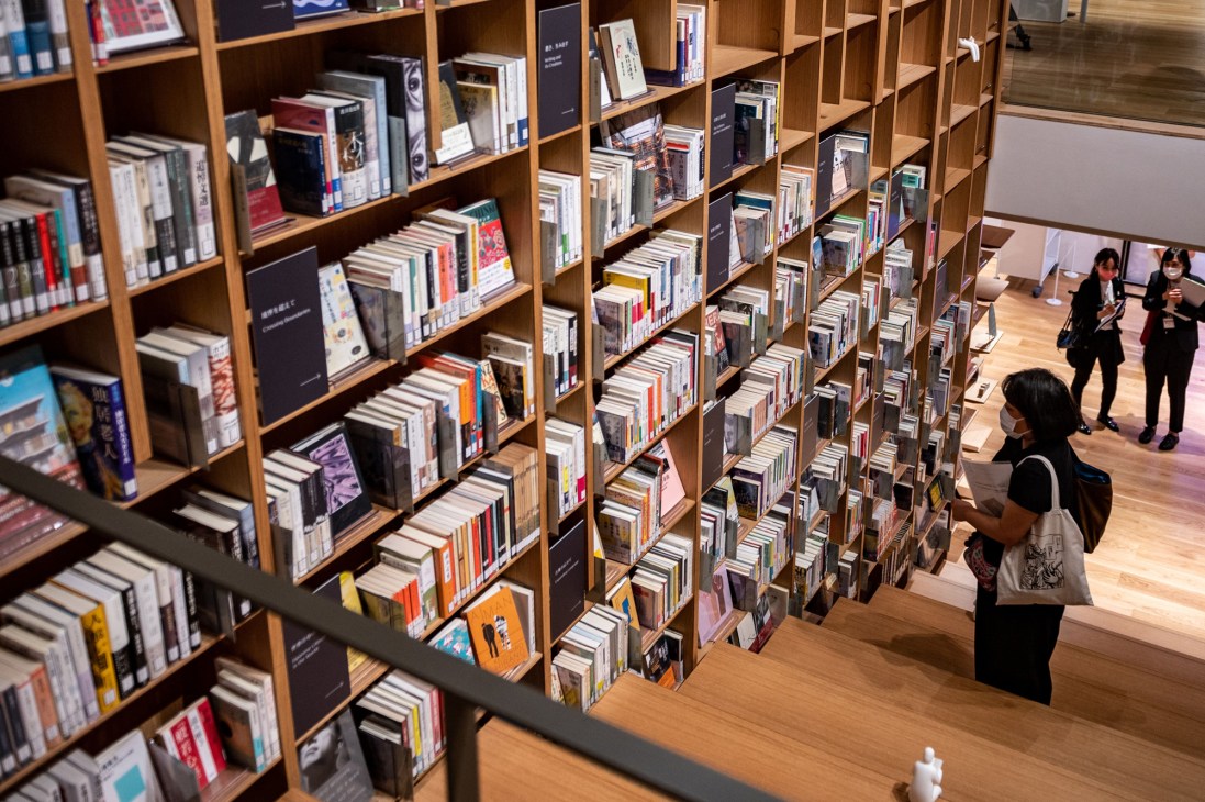 Visitors browsing books on wooden shelves in the Haruki Murakami Library's modern interior space