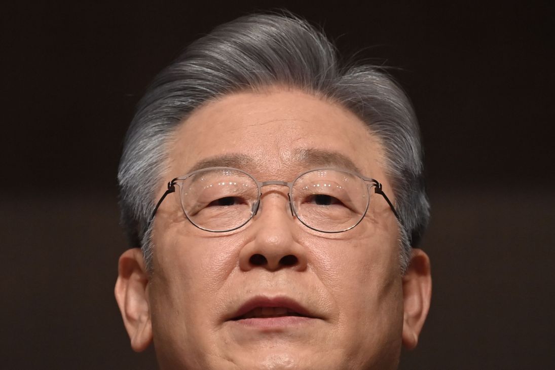 Older Asian man with gray hair and wire-rimmed glasses speaking at what appears to be a formal event