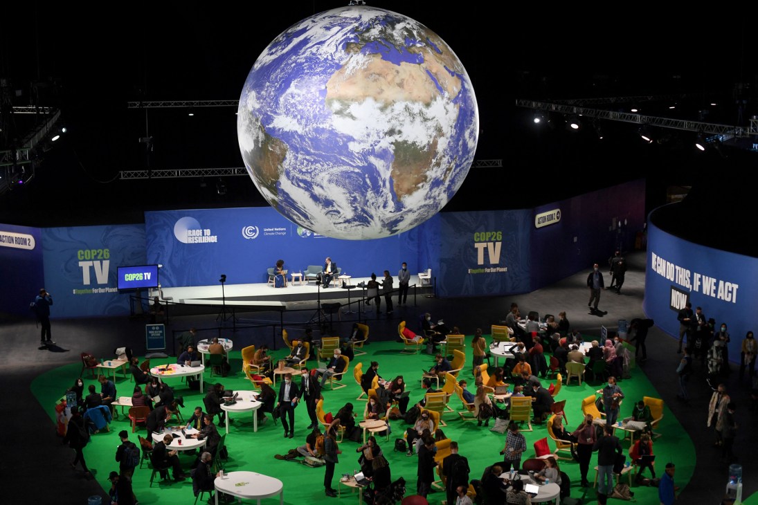 Large suspended Earth globe display above seated attendees at COP26 climate conference venue with blue signage
