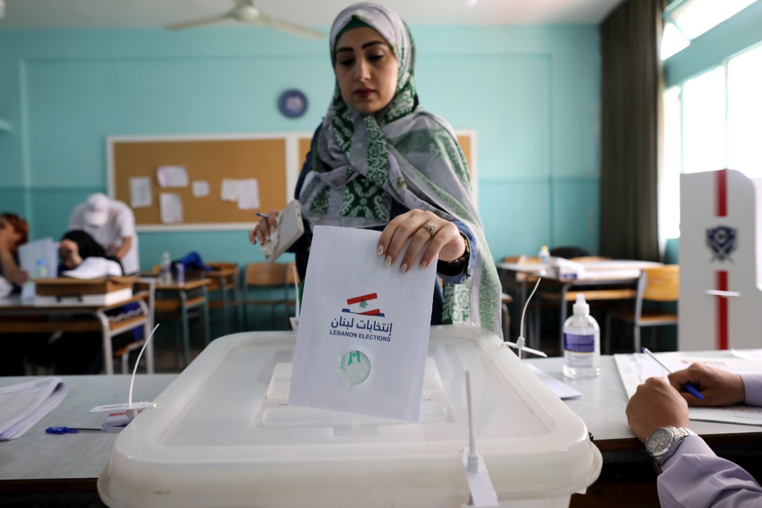 Woman in hijab casting ballot into transparent election box in Lebanese polling station