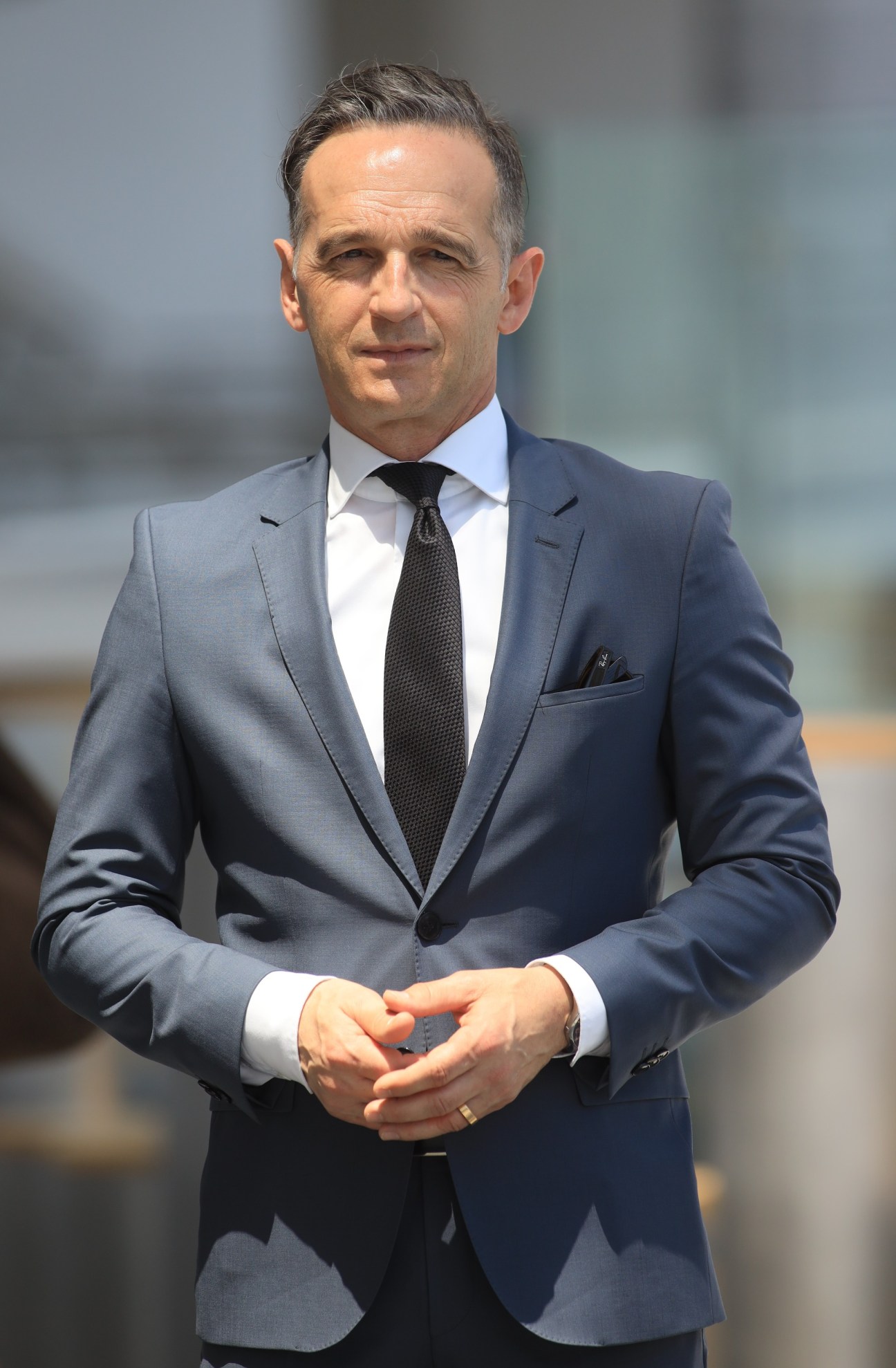 Heiko Maas in a grey suit and dark tie standing with hands clasped
