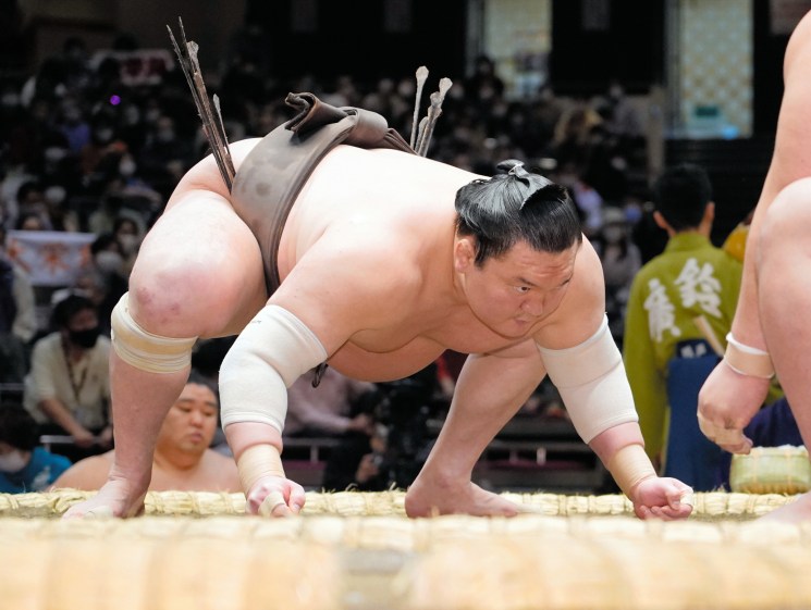 Two sumo wrestlers grappling during a match on a sandy ring with spectators in the background