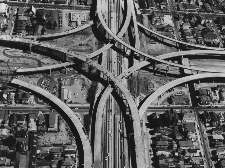 Aerial black and white view of complex highway interchange with multiple curved overpasses intersecting through urban area