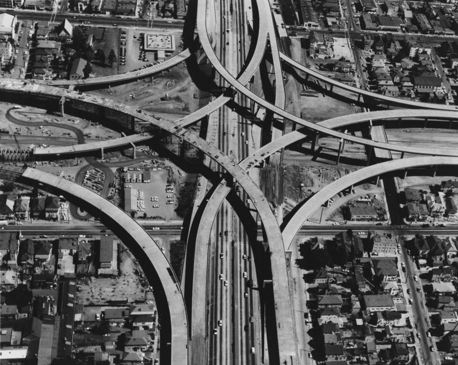 Aerial black and white view of complex highway interchange with multiple curved overpasses intersecting through urban area