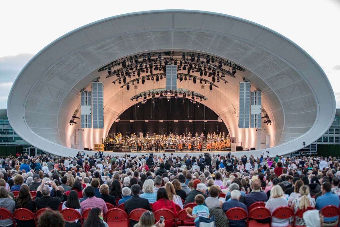 The Rady Shell outdoor amphitheater with curved white canopy and orchestra performing to large seated audience