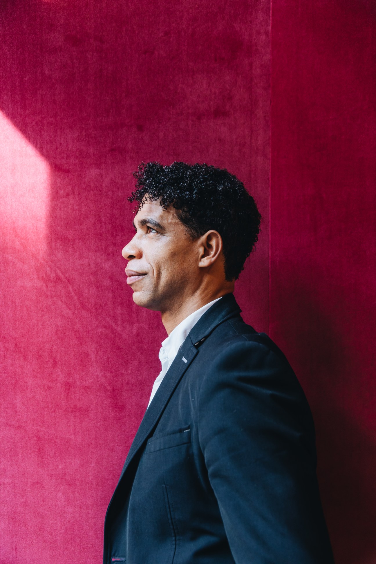 Profile view of a man in a dark suit against a vibrant red background