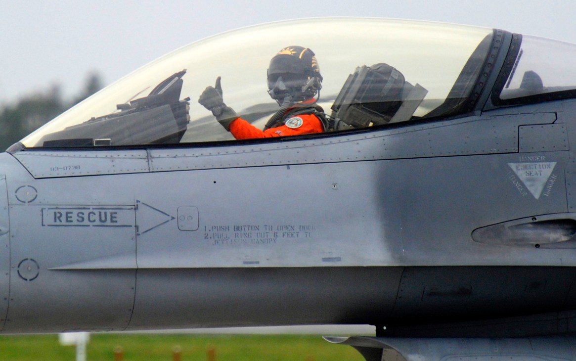 Military pilot in cockpit of fighter jet giving thumbs up gesture
