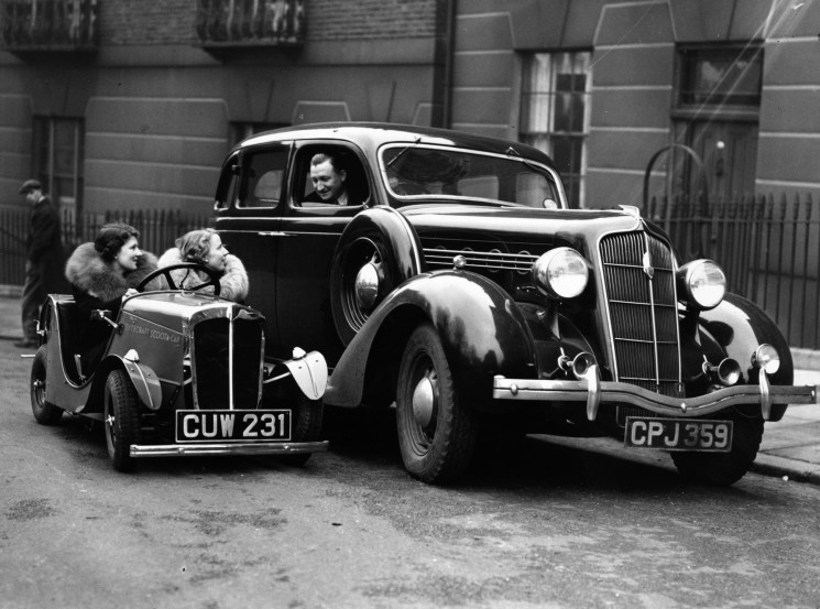 Two women in a small Rytecraft Scootacar miniature vehicle next to a regular car on a London street