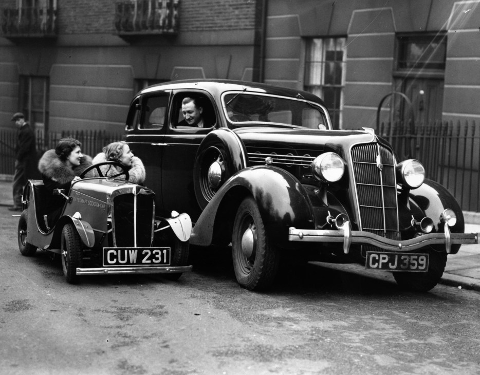Two women in a small Rytecraft Scootacar miniature vehicle next to a regular car on a London street