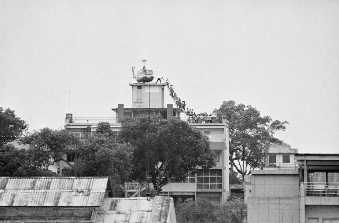 Embassy building exterior with helicopter on roof and people evacuating down stairs
