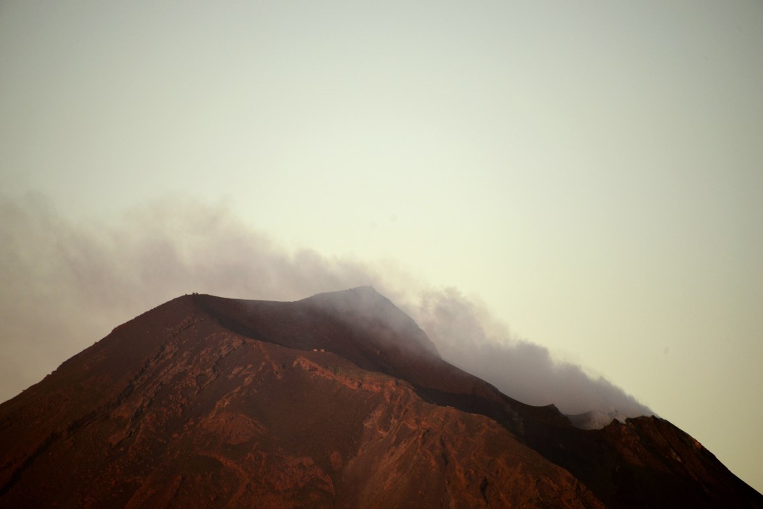Volcanic mountain peak with smoke or steam rising from crater under overcast sky
