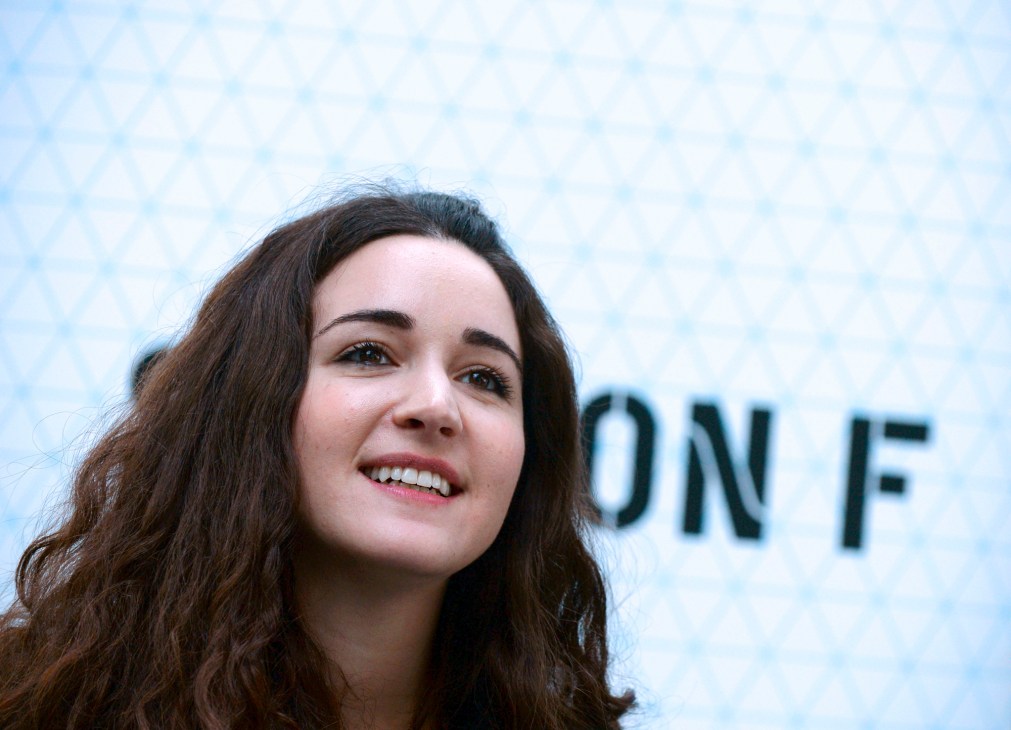 Woman with long dark hair smiling against a light blue geometric patterned background