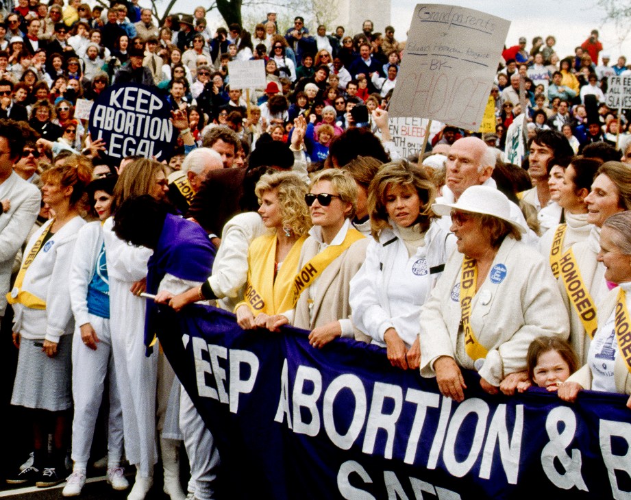 Jane Fonda at pro-choice rally in 1989 holding banner with other protesters wearing white and yellow sashes