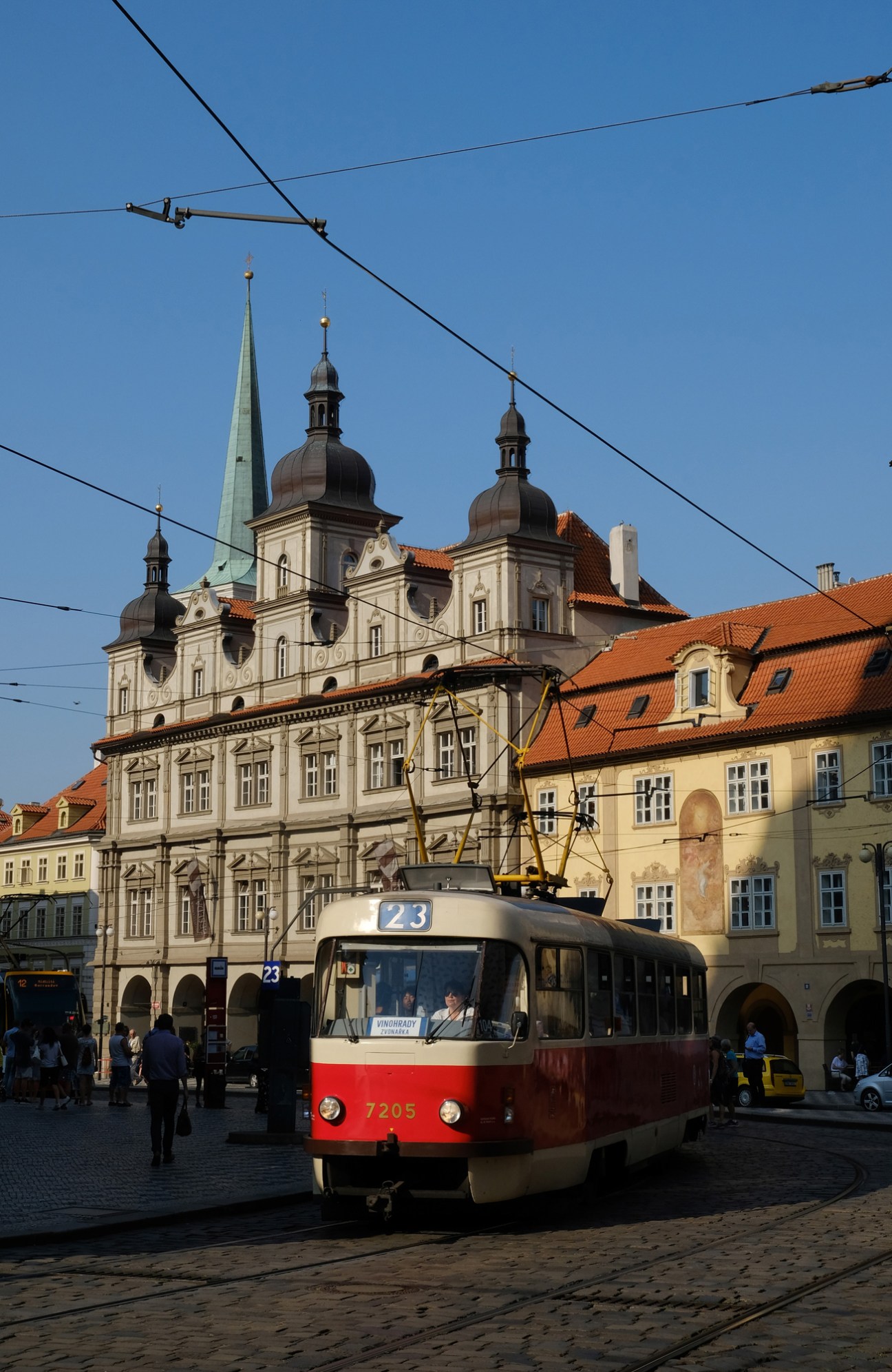 Red and white tram on cobblestone square with historic baroque buildings and church spires in Prague