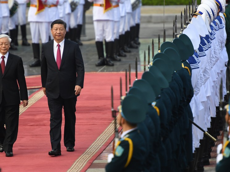 Two men in dark suits walking on red carpet past military honor guard