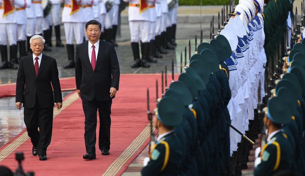 Two men in dark suits walking on red carpet past military honor guard