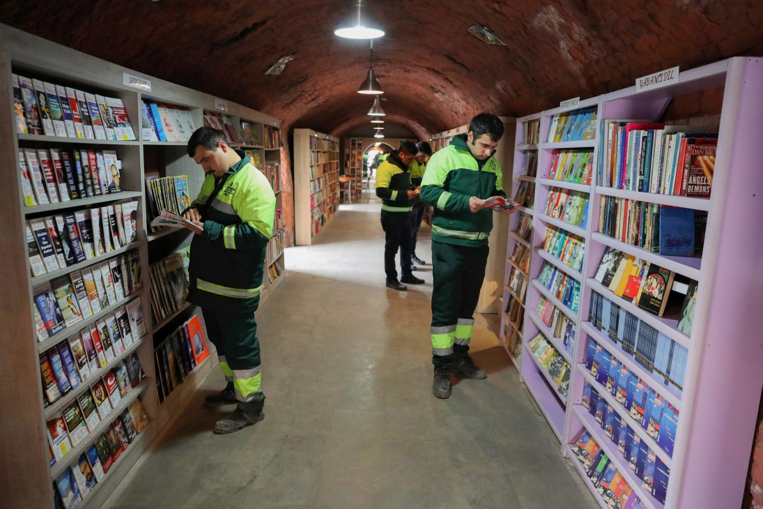 Sanitation workers in high-visibility vests browse books in Ankara's library for discarded publications.