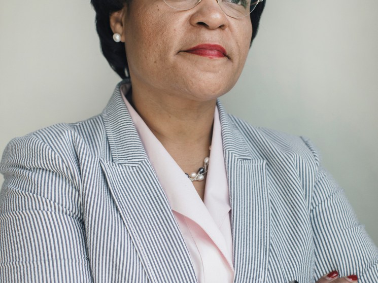 Woman in professional attire wearing glasses and jewelry, posed against a neutral background.