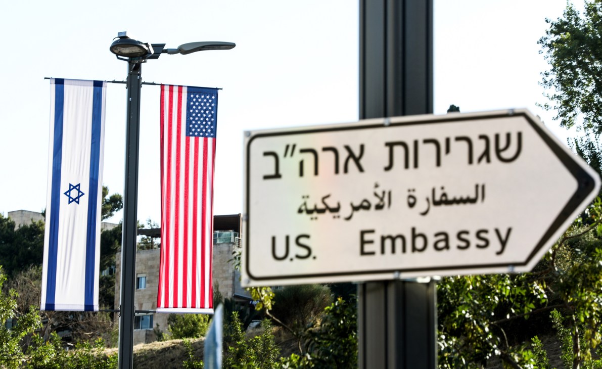 Road sign pointing to U.S. Embassy in Hebrew, Arabic and English with Israeli and American flags hanging nearby