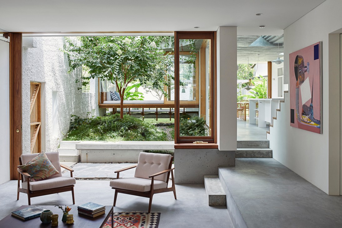 Modern living room with concrete walls, wood-framed sliding doors opening to a lush courtyard with crepe myrtle tree.