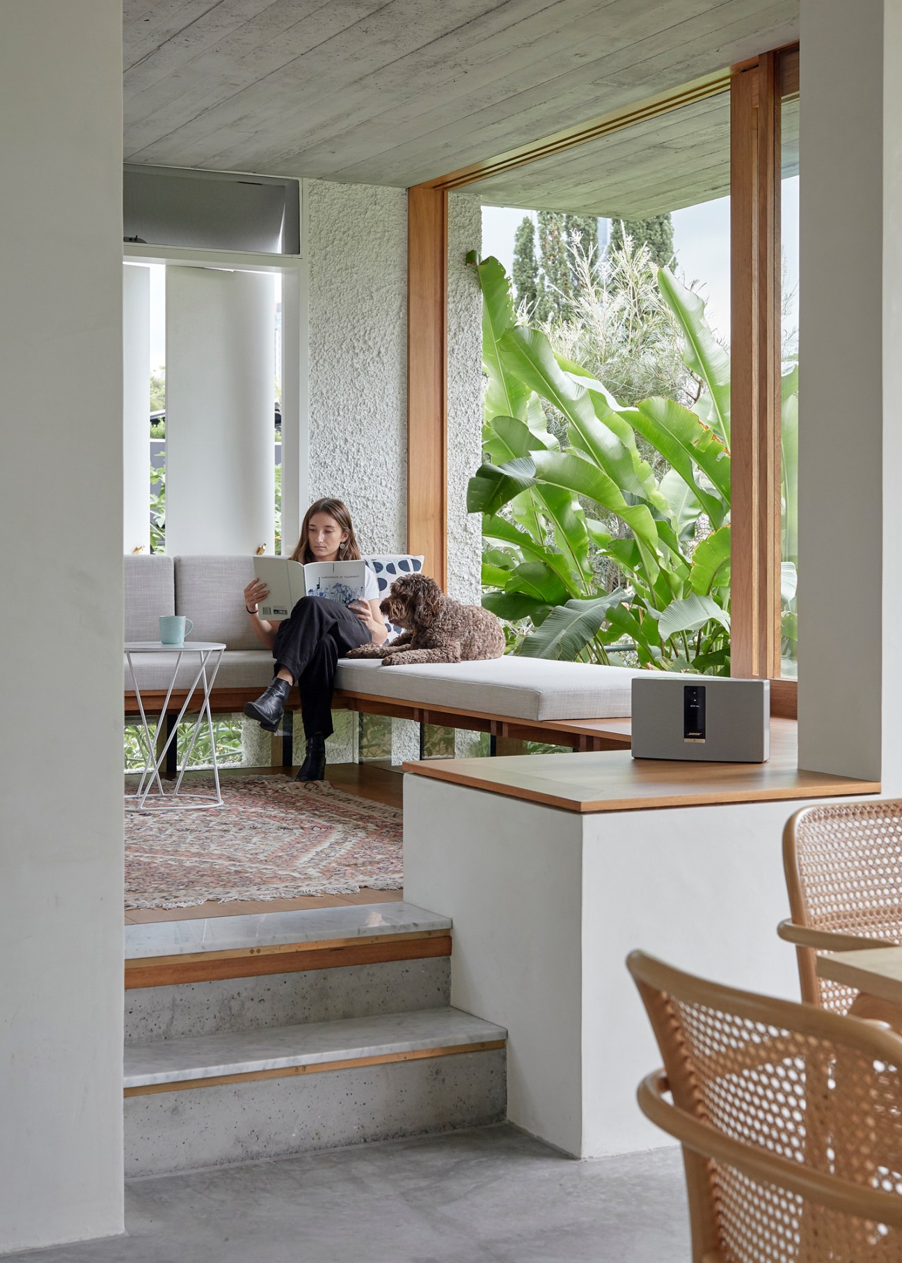 Person reading while sitting on built-in bench with dog beside them in modern living room