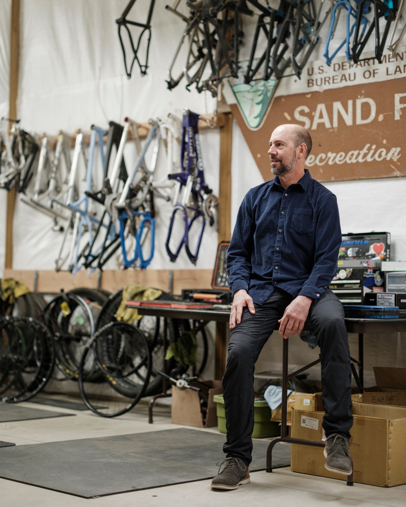 Lance Canfield sitting in his bike workshop surrounded by bicycle frames and equipment
