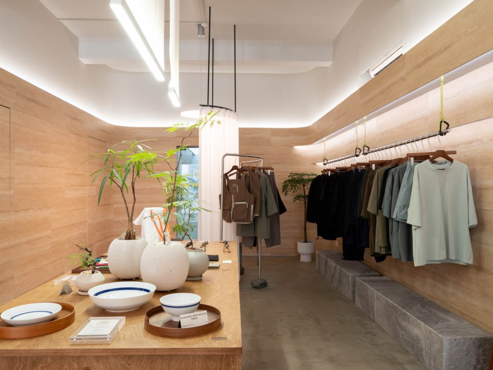 Modern retail interior with wooden walls, clothing racks displaying neutral-toned garments, and white planters
