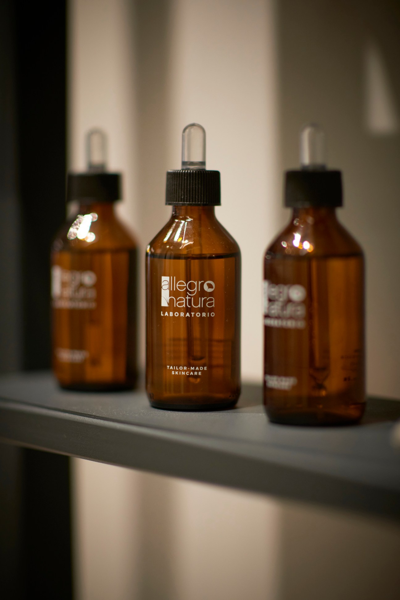 Three amber glass dropper bottles with black caps from Allegro Natura cosmetics brand on a shelf