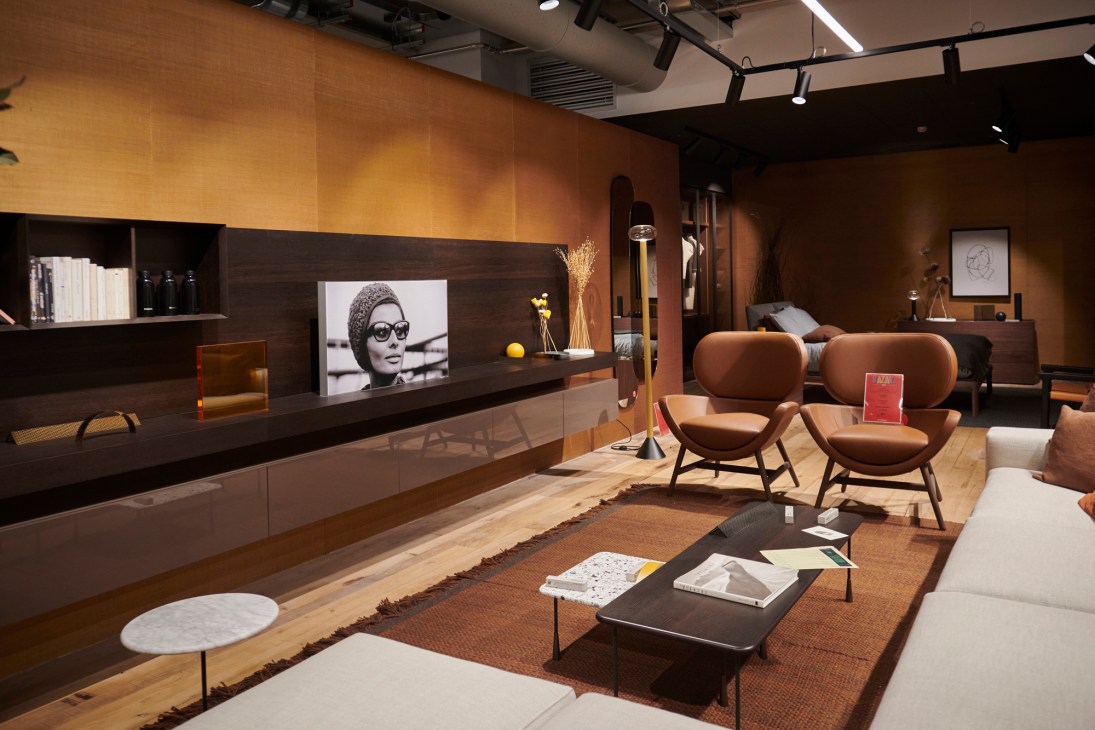 Modern furniture showroom with brown leather chairs, dark wood entertainment unit, and warm lighting